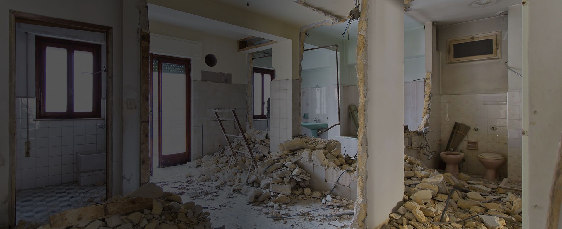 Das Innere eines teilweise zerstörten Raums mit auf dem Boden verstreuten Trümmern, die Rohre und baufällige Wandteile freilegen.